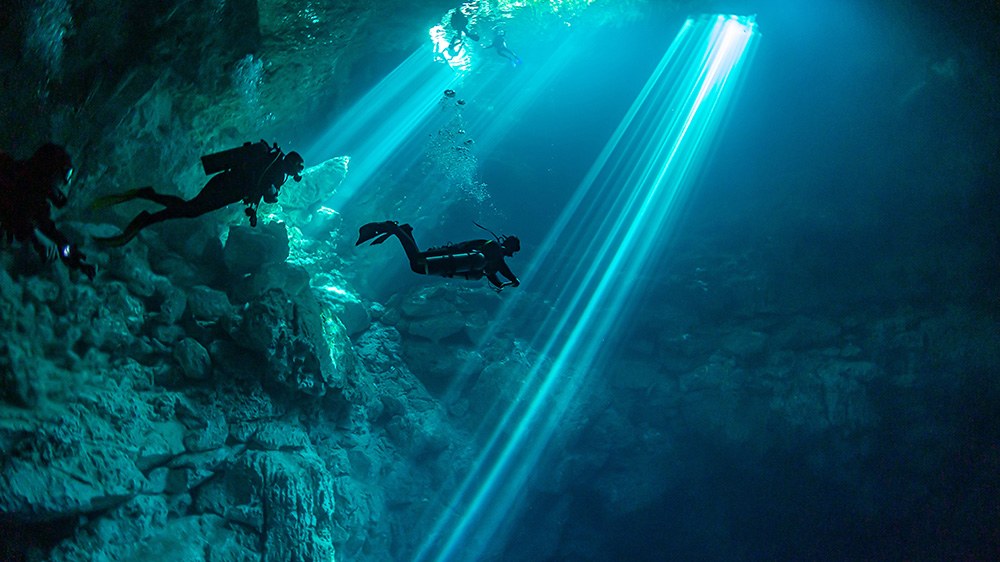 Taucher in einer Unterwasserhöhle mit einfallenden Lichtstrahlen als Motiv für anspruchsvolle Tauchgänge und gute Vorbereitung.